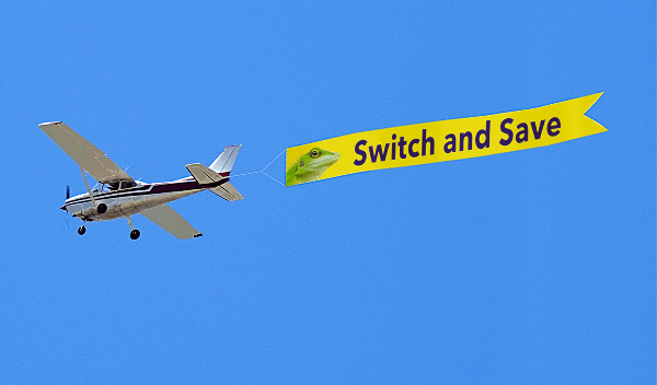 Airplane pulling a yellow advertisement banner that says switch and save banner behind it in the air.