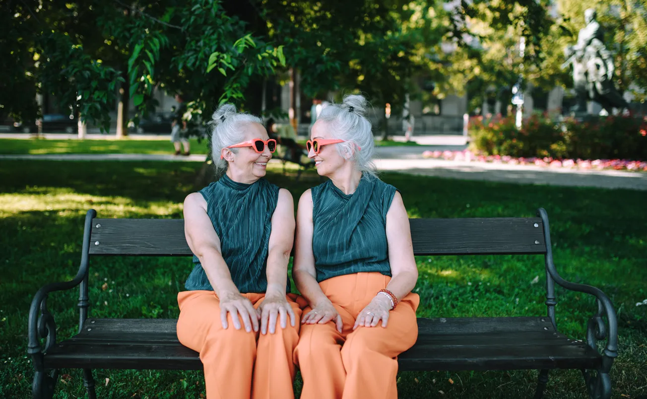 Happy senior sisters wearing the same outfit and sitting in city park and resting