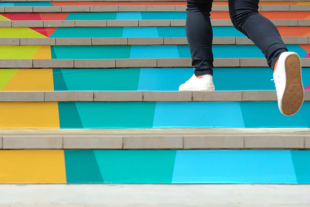 Lower part of teenage girl in casual shoe walking up outdoor colorful stair