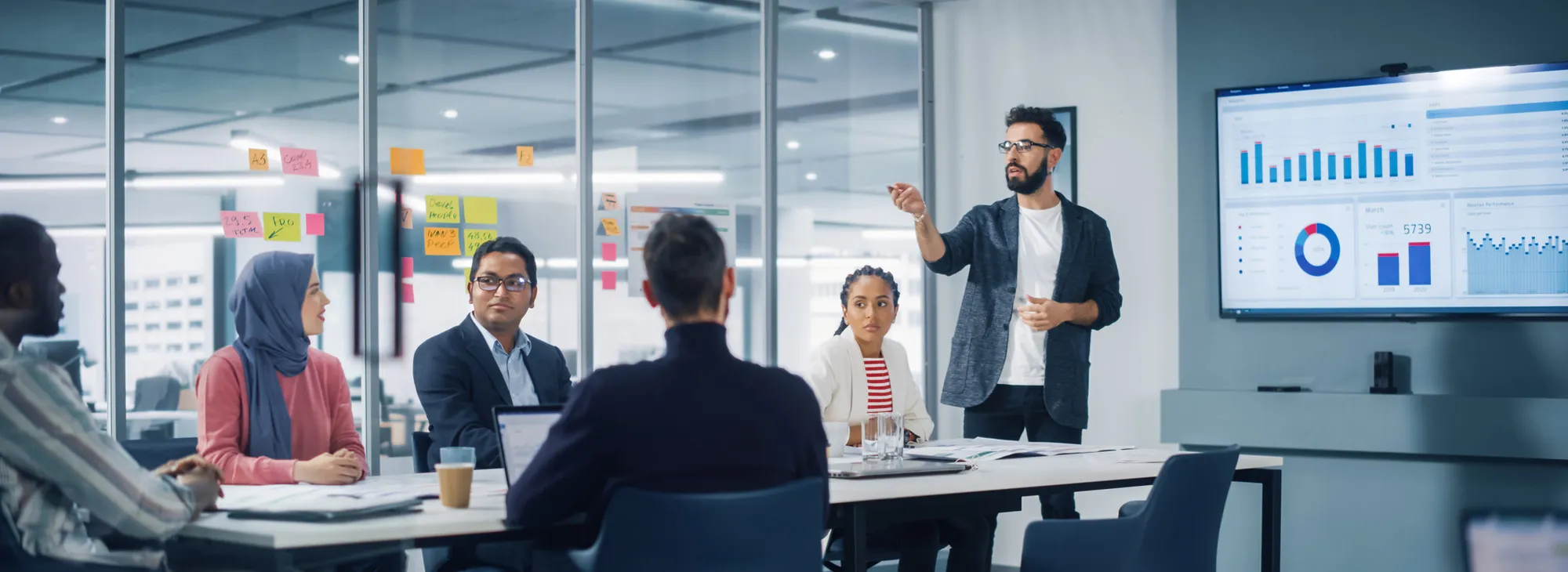 Diverse Modern Office: Businessman Leads Business Meeting with Managers, Talks, uses Presentation TV with Statistics, Infographics