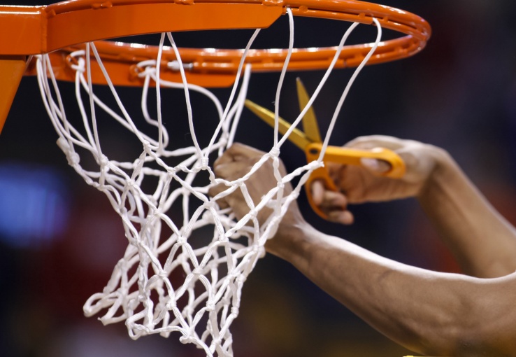 A pair of hands cutting down a basketball net during a championship celebration.