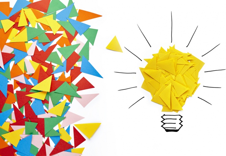 Scraps of colorful paper in a pile on the left and yellow scraps of paper in the form of a light bulb on the right.