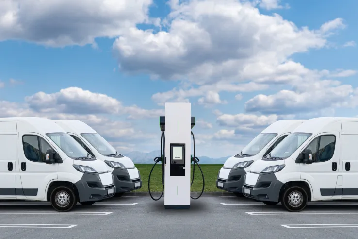 Rows of electric delivery vans parked near charging stations, representing the rising demand among utility companies and industrial customers for clean transportation as part of a net zero future and sustainable business models.