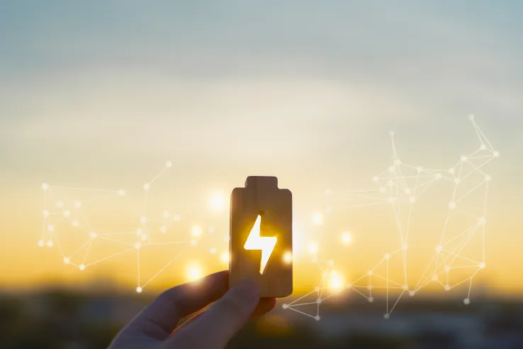 Renewable energy concept with hand holding wooden battery icon glowing at sunset. Symbol of clean energy, power storage, sustainability, future technology, green innovation, and energy management.