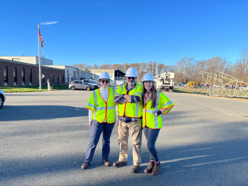 Team of three wearing white hard hats, yellow safety vests, and steel-toed boots