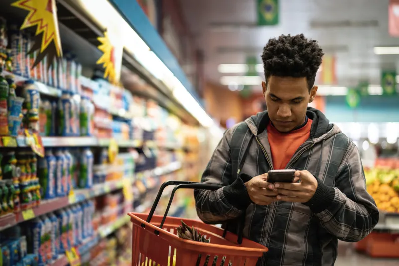 Person shopping in a grocery aisle while using a phone, representing in-store app behavior and customer engagement 