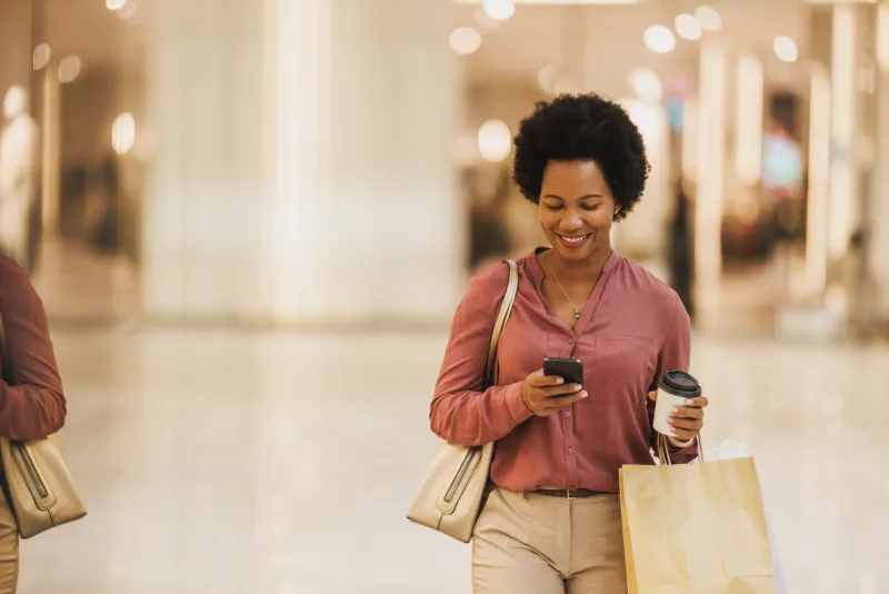 Shopper walking with bags while using a phone, representing retail engagement and expanding customer appeal